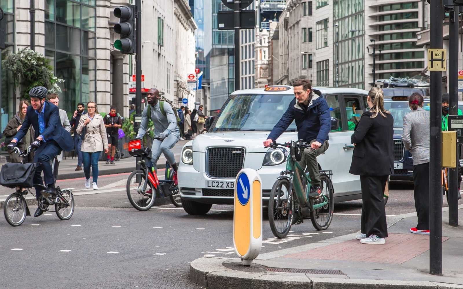 pedestrians walking and biking past taxi cabs on their london commute